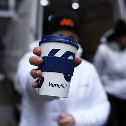 Person hält einen Kaffeebecher mit kununu Logo in die Kamera